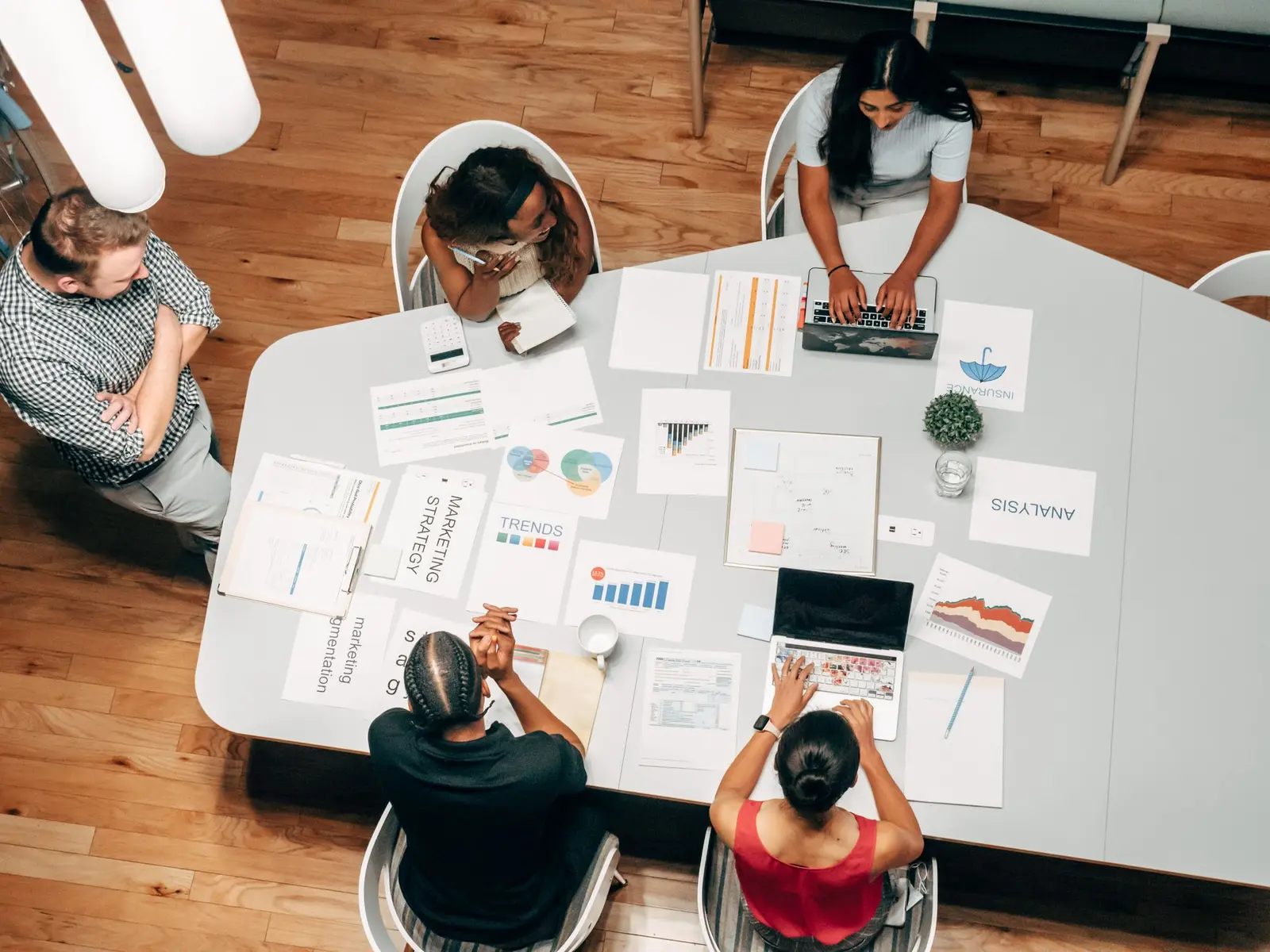 Overhead view of a team working at a white table covered in printed campaign plans and charts